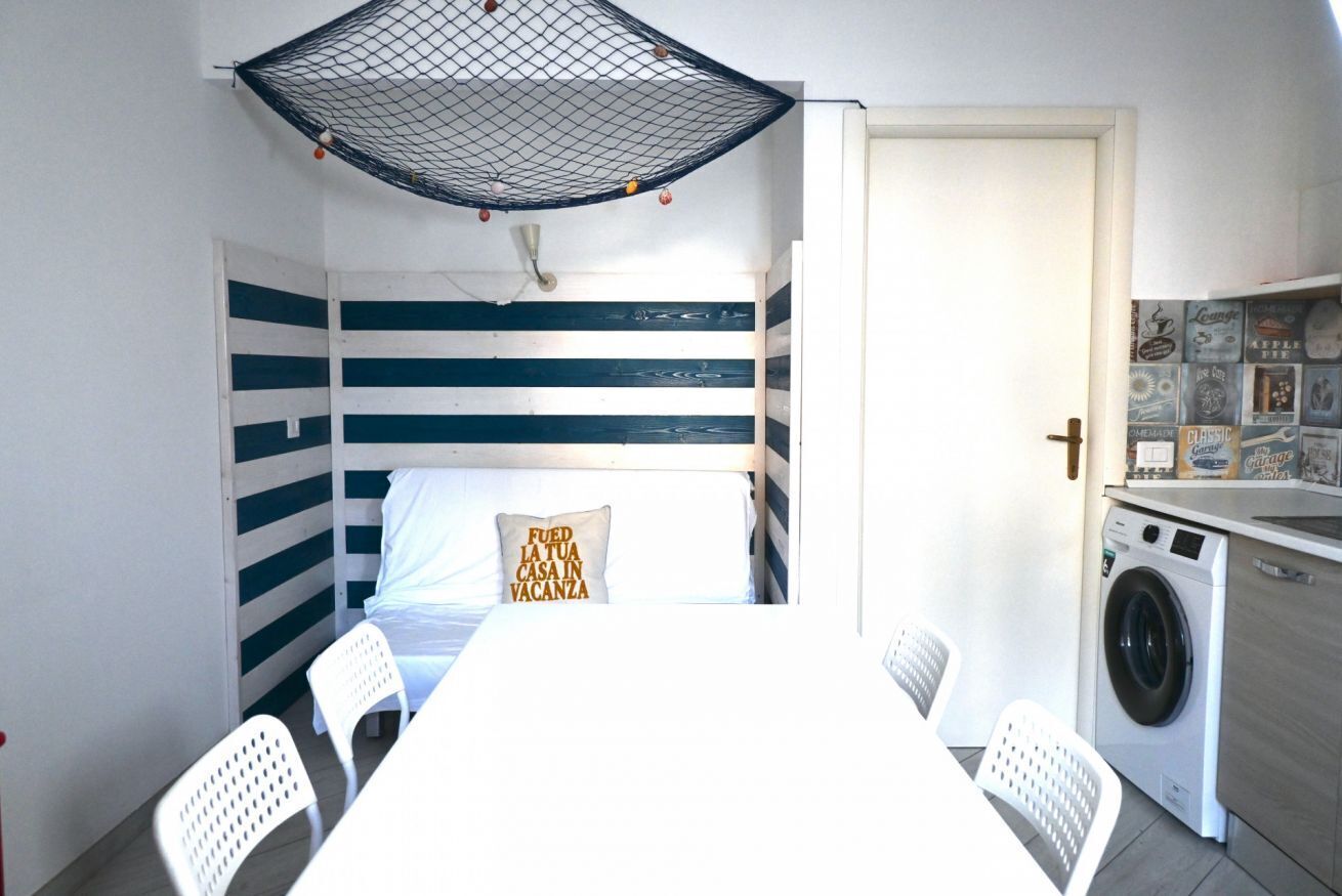 Ein kleines Zimmer mit Bett, Tisch, Stühlen, einer Waschmaschine und einem Moskitonetz an der Decke.