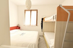 A single-bed room with a bunk bed, a window with curtains, a bedside table with a lamp, and a mirror on the wall.