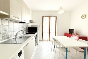 A kitchen with a sink, stove, and cabinets, a dining table with chairs, and a television on a red cabinet.
