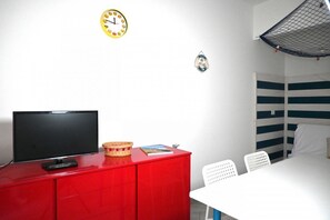 A room with a television on a red cabinet, a clock on the wall, and a bunk bed with a net canopy.