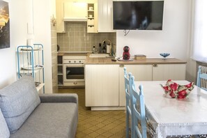 A compact kitchen with a dining area, a sofa, and a TV mounted on the wall.