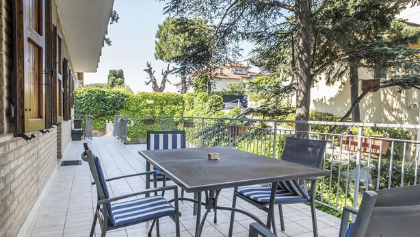 Un balcone con tavolo e sedie, un pavimento piastrellato e vista su un giardino e degli edifici.