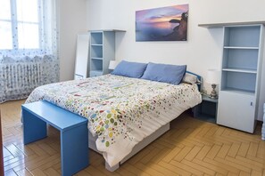 A bedroom with a bed, a bench, a white wardrobe, and a shelf unit.