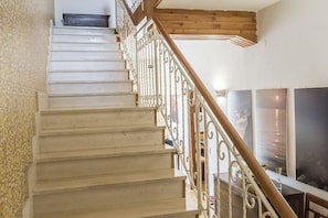 A staircase with a wooden handrail and white balusters, leading to a room with a large window and a flat-screen TV.