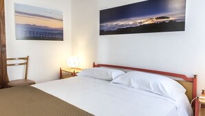 Un lit avec du linge de lit blanc, une tête de lit en bois, une table de chevet avec une lampe et deux tableaux accrochés au mur.