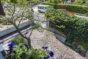 A stone-paved outdoor area with a metal fence, a tree, and a red car parked on the street.