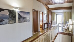Un couloir avec un plafond en bois, un escalier doté d’une rampe et une vue sur une pièce avec une fenêtre.