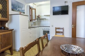 Une cuisine avec des meubles blancs, une table à manger en bois et un téléviseur fixé au mur.