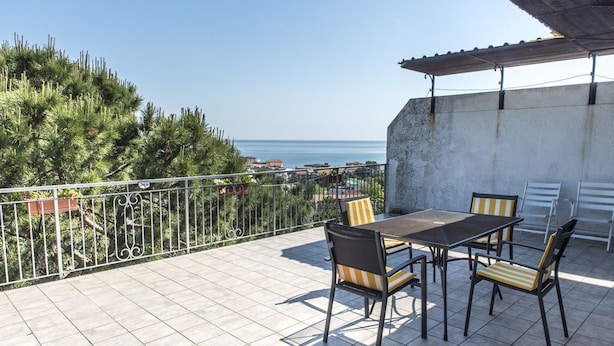 Une terrasse avec une table et des chaises, une vue sur la mer et une rambarde.