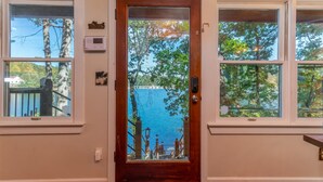 Uma porta de madeira com um painel de vidro, duas janelas de cada lado e vista para um lago e árvores.