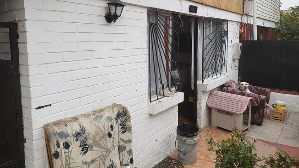 A white brick building with a wooden upper section, a black gate, and a small garden area with a metal bucket and a bench. - Family atmosphere 20 (Viña)