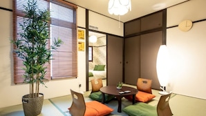 A traditional Japanese-style room with tatami flooring, a low table with cushions, a potted plant, and sliding doors. - R-Guest Residence (Osaka)