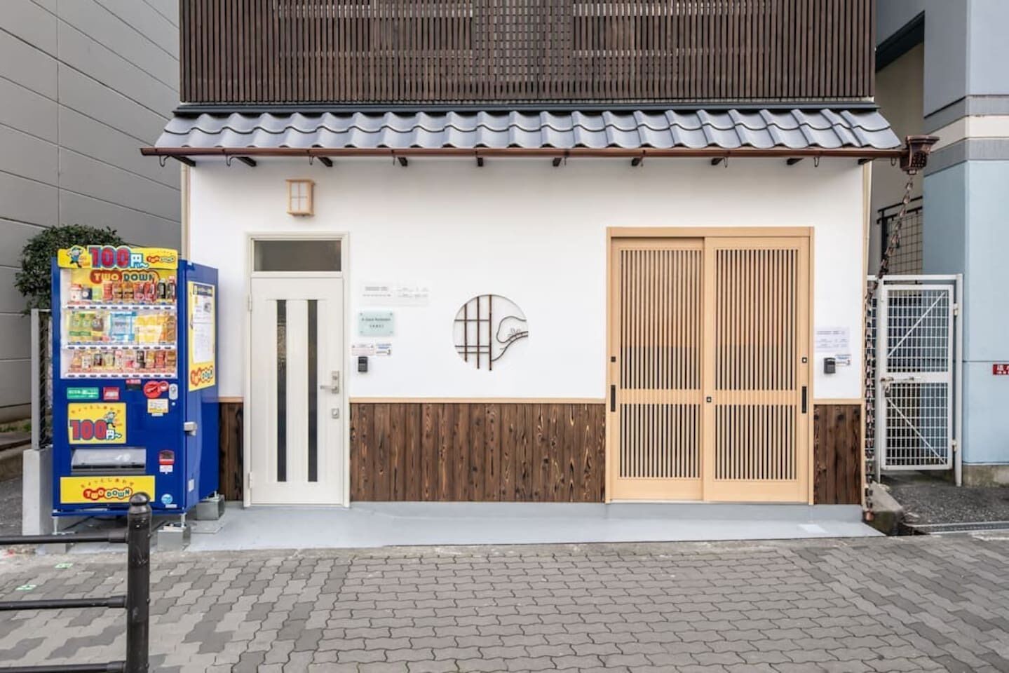 En byggnad med en traditionell japansk entré, en försäljningsautomat och en trädörr.