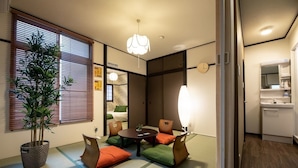 A compact hotel room with a tatami mat floor, a dining table with chairs, a potted plant, and a modern light fixture. - R-Guest Residence (Osaka)