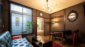 A modern living room with a leather sofa, a glass coffee table, a dining area with a table and chairs, and a large mirror on the wall. - R-Guest Residence (Osaka)