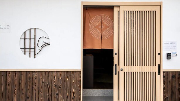 A traditional Japanese entrance with a sliding door, a circular wall decoration, and a wooden panel design. - R-Guest Residence (Osaka)