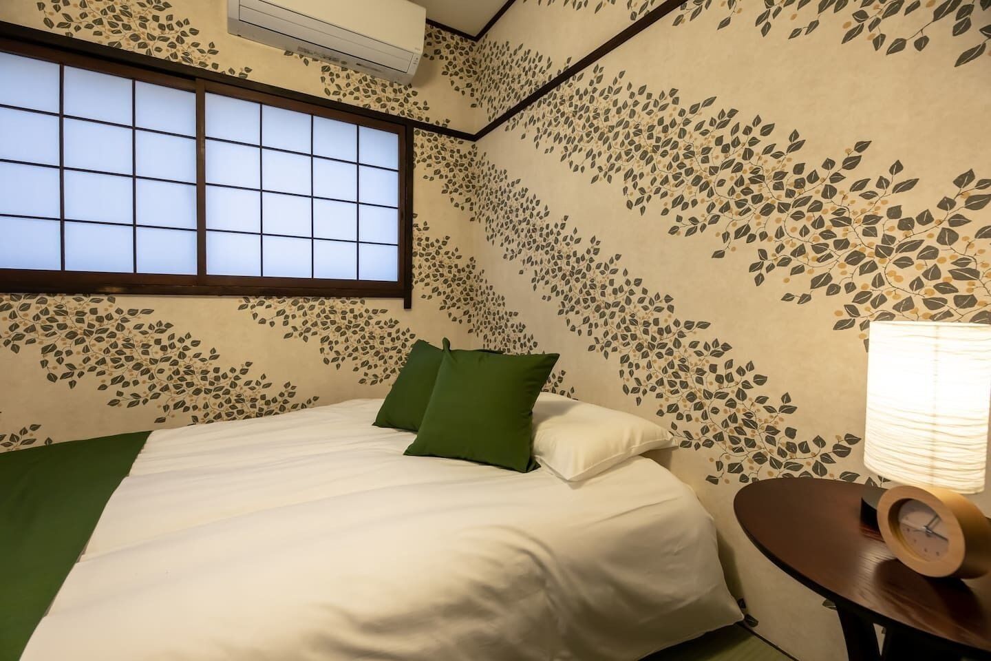 Um quarto com uma cama, uma janela e uma parede com um desenho de folhas.