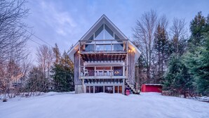 A modern two-story building with a triangular roof, large windows, and a wooden deck. - Classic Stowe Ski 3 Bedroom Chalet by RedAwning (Stowe)