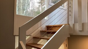 A modern staircase with wooden steps and white railings, leading to a room with a large window overlooking trees. - Classic Stowe Ski 3 Bedroom Chalet by RedAwning (Stowe)