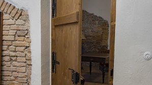 Een houten deur die leidt naar een kamer met een stenen muur en een houten tafel.