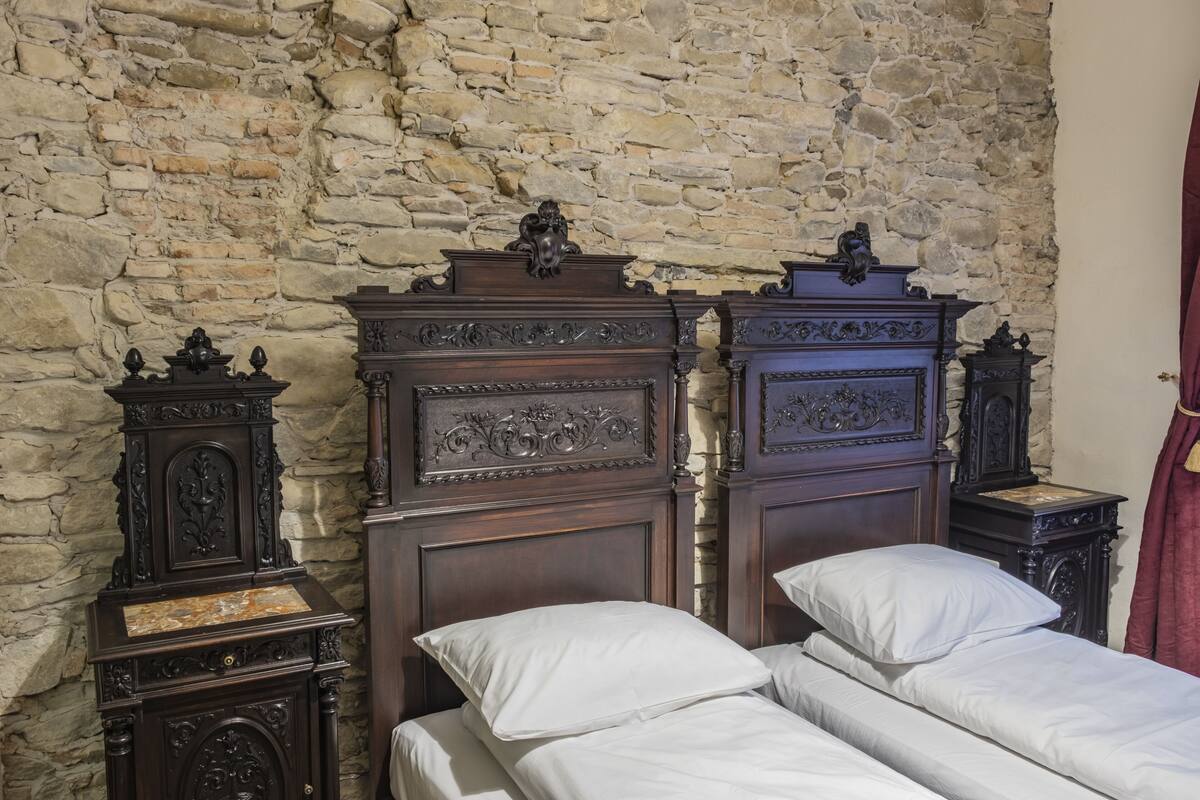 A room with a stone wall, a wooden bed with white bedding, and two nightstands with decorative carvings.