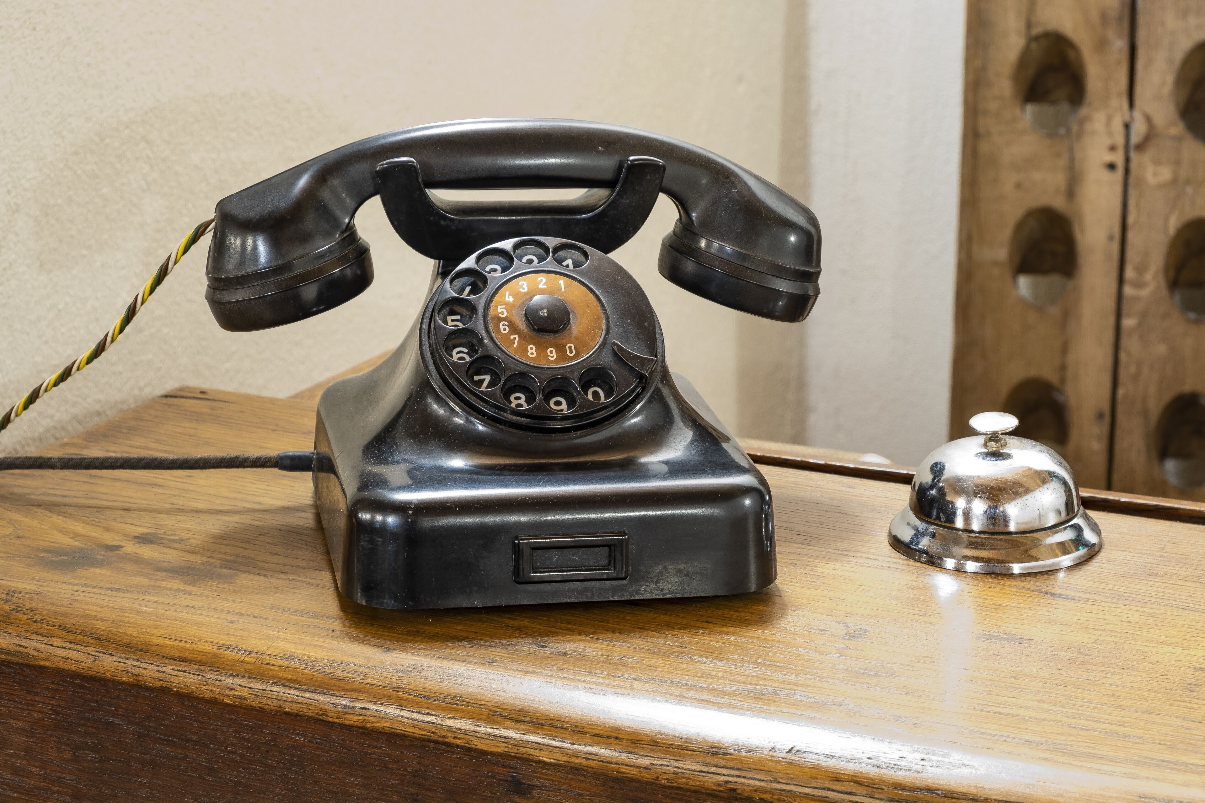 A vintage rotary dial telephone on a wooden desk with a metal bell.