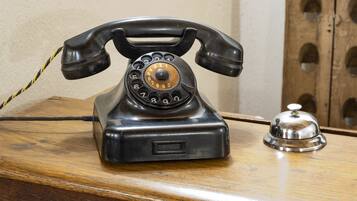 A vintage rotary dial telephone on a wooden desk with a metal bell.