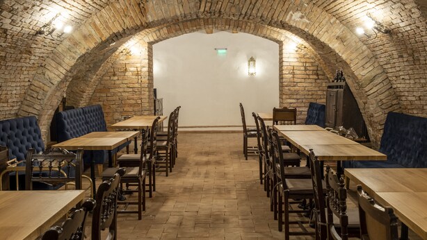 Een restaurant met een plafond van bakstenen bogen, houten tafels en stoelen, en blauwe gestoffeerde zitbanken.