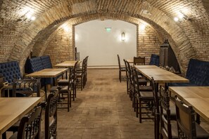 Een restaurant met een plafond van bakstenen bogen, houten tafels en stoelen, en blauwe gestoffeerde zitbanken.