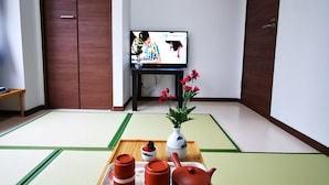 Una habitación japonesa tradicional con suelo de tatami, un televisor, una bandeja con teteras y un jarrón con flores.