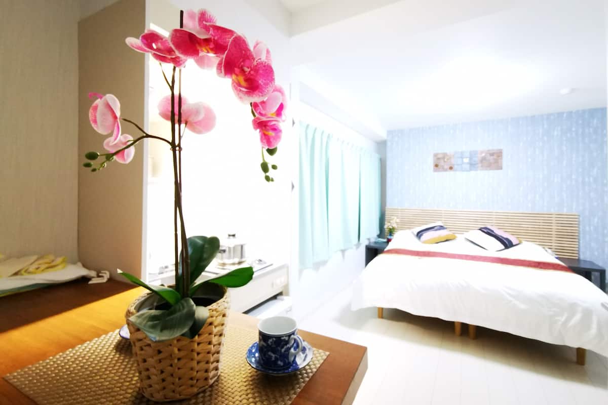 Quarto de hotel com uma cama, uma mesa de cabeceira com chávena e pires, uma orquídea num vaso e vista para outro quarto.