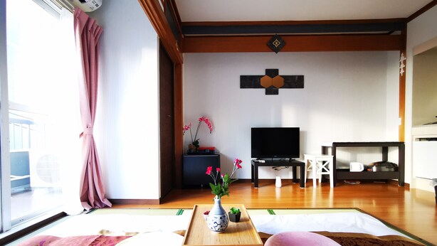Una sala de estar con esteras de tatami, un televisor, una mesita con un florero y un sofá.