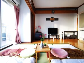 Ein Wohnzimmer mit Tatami-Matten, einem Fernseher, einem kleinen Tisch mit einer Vase und einem Sofa.