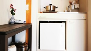 Una cocina compacta con lavavajillas integrado, un refrigerador pequeño y una estantería con utensilios de cocina.