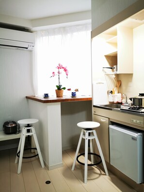 A compact kitchen with a small dining area, a refrigerator, and a window with a potted orchid.
