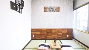 Una habitación con esteras de tatami, un muro de madera bajo, una mesa pequeña con un florero y cojines.