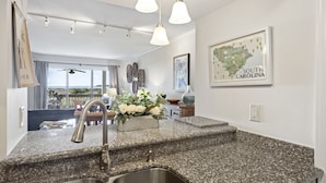 A kitchen with granite countertops, stainless steel sink, pendant lights, and a view of the outdoors.