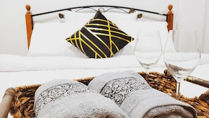 Un lit bien fait, avec un oreiller noir et jaune, deux verres d’eau et un panier en osier contenant des serviettes.