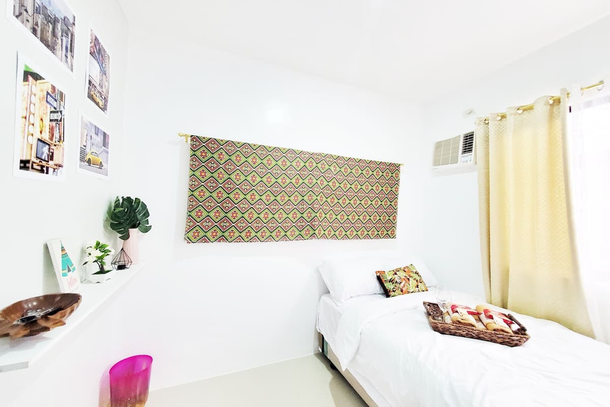 Een slaapkamer met een bed, wandtapijt, een kamerplant en een plank met decoratieve objecten.