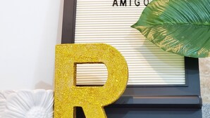 A decorative sign with "WELCOME TO BALA AMIGO" and a large glittery gold 'R' in front.