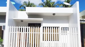 A white building with a white picket fence, a small overhang, and a window with curtains.