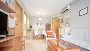 Un salon moderne avec un téléviseur à écran plat, des meubles en bois, une table basse en verre et un canapé blanc.