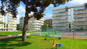 Un parc avec une aire de jeux, un court de tennis et un arbre.