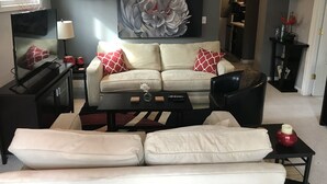 A living room with a beige sofa, red and white patterned pillows, a black coffee table, and a large abstract painting on the wall. - Spacious suite with private patio, minutes from DC / DCA (Arlington)