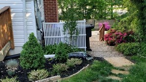 A well-maintained garden with a stone pathway, a white picket fence, and various shrubs and plants. - Spacious suite with private patio, minutes from DC / DCA (Arlington)
