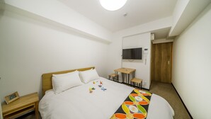 A hotel room with a bed, a desk, a chair, a TV, and a door.
