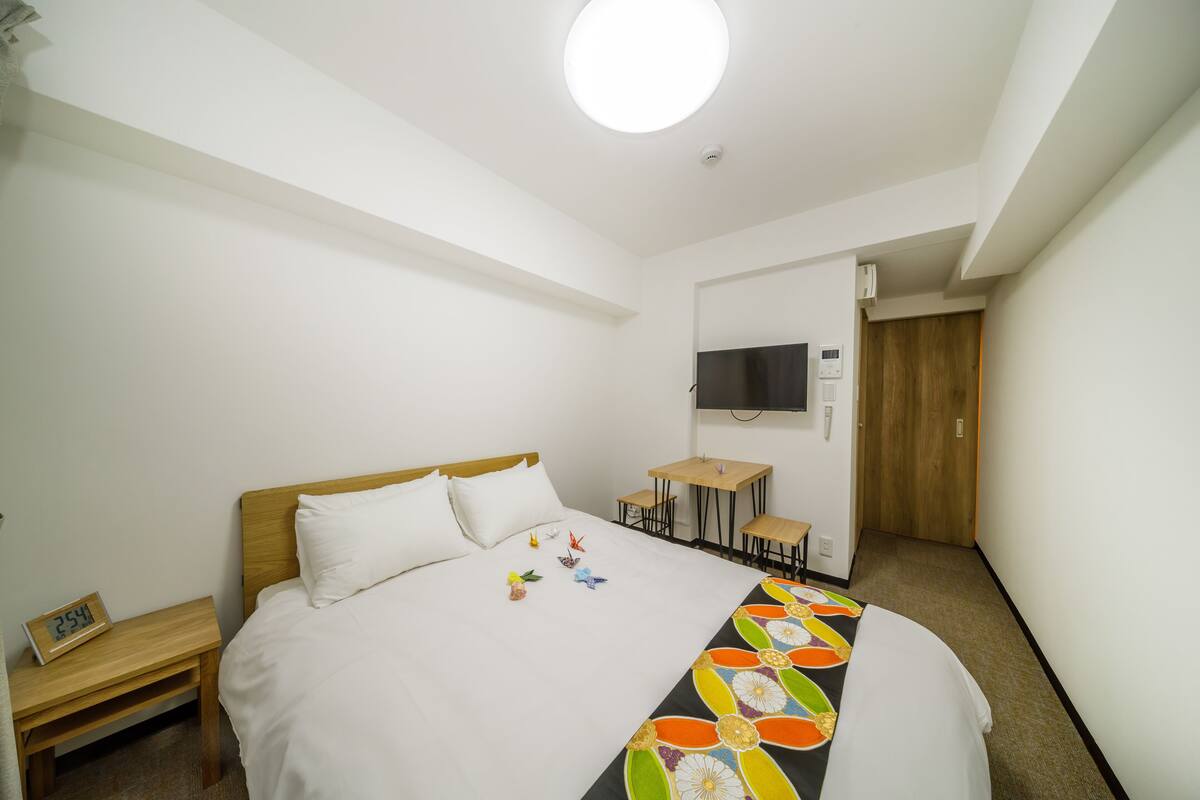 A hotel room with a bed, a desk, a chair, a TV, and a door.