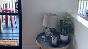 Een kamer met houten vloer, een klein rond tafeltje met een lamp, een potplant en een poster van Nieuw-Zeelandse vogels.
