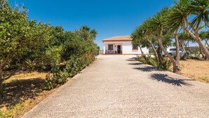 A pathway leading to a white building with a tiled roof, surrounded by greenery and palm trees. - Charming Home with Pool, Spacious Terrace, Garden & Wi-Fi; Pets Allowed, Parking Available (Conil de la Frontera)