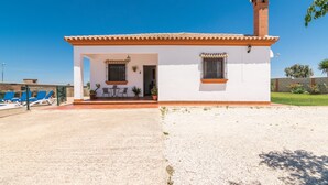 A single-story building with a tiled roof, a small porch, and a gravel driveway. - Charming Home with Pool, Spacious Terrace, Garden & Wi-Fi; Pets Allowed, Parking Available (Conil de la Frontera)